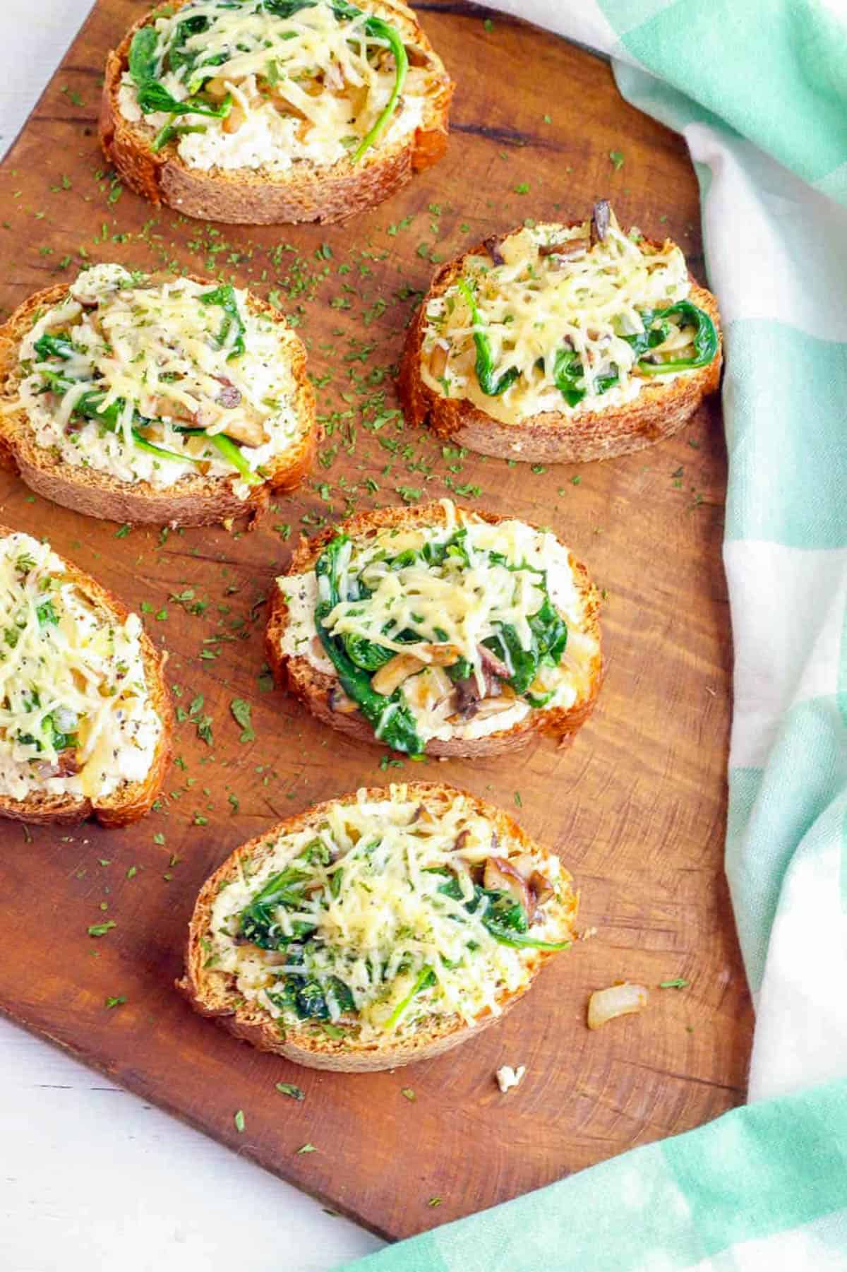 Mushroom toast with spinach and roasted garlic on a wooden cutting board.