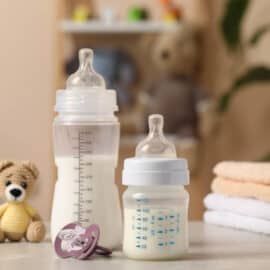 Feeding bottles with baby formula, pacifier, toys and towels on light grey table indoors.