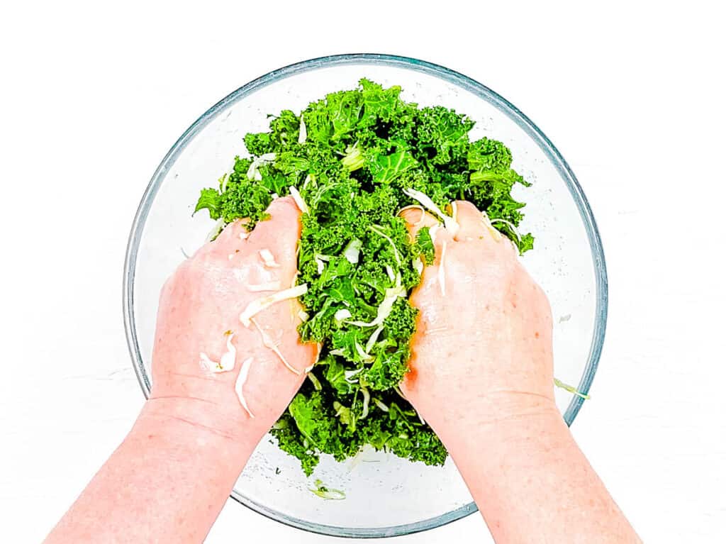 Hands massaging kale in a mixing bowl.