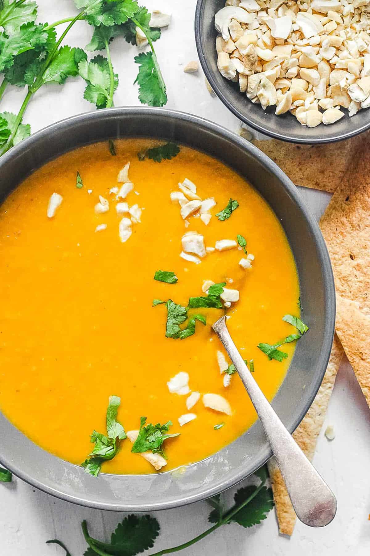 Overhead shot of a white bowl of curried butternut squash soup with a soon, nuts, and herbs.