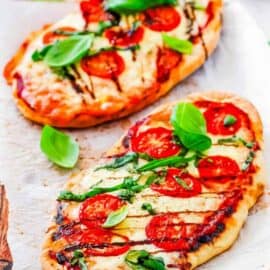 Margherita flatbread pizzas on a wooden cutting board, topped with basil, tomatoes and mozzarella.
