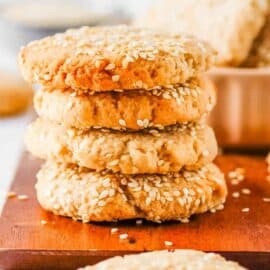 Sesame tahini cookies stacked on a wooden cutting board.