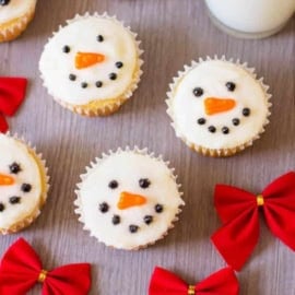 Decorated snowman cupcakes against a grey background with a glass of milk on the side.