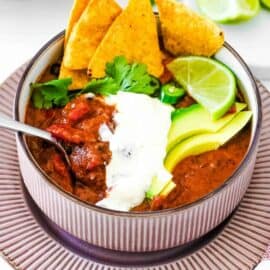Easy vegan black bean soup, served in a grey bowl, garnished with cilantro, lime, avocado, crema, and corn chips.