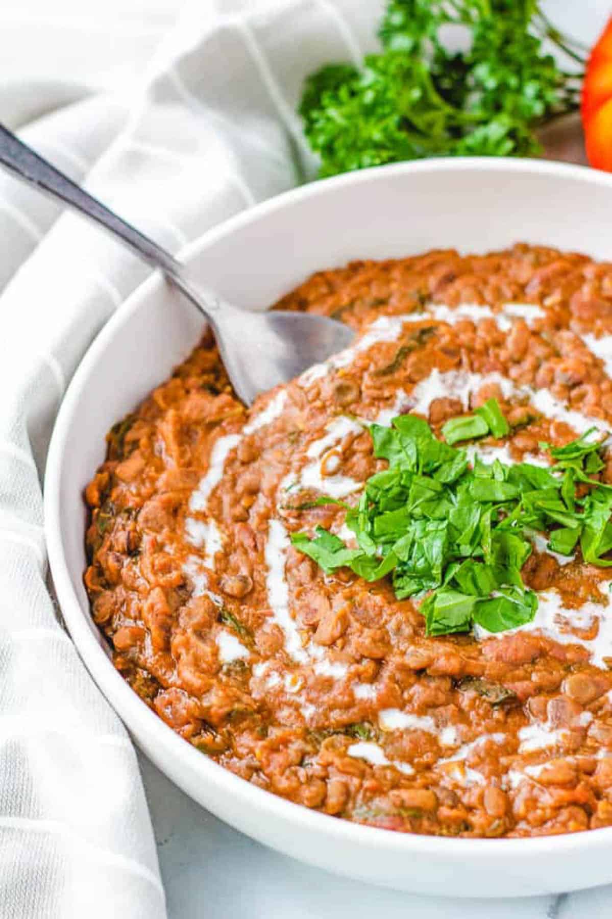 Close up side s،t of a bowl of dal makhani with herbs.