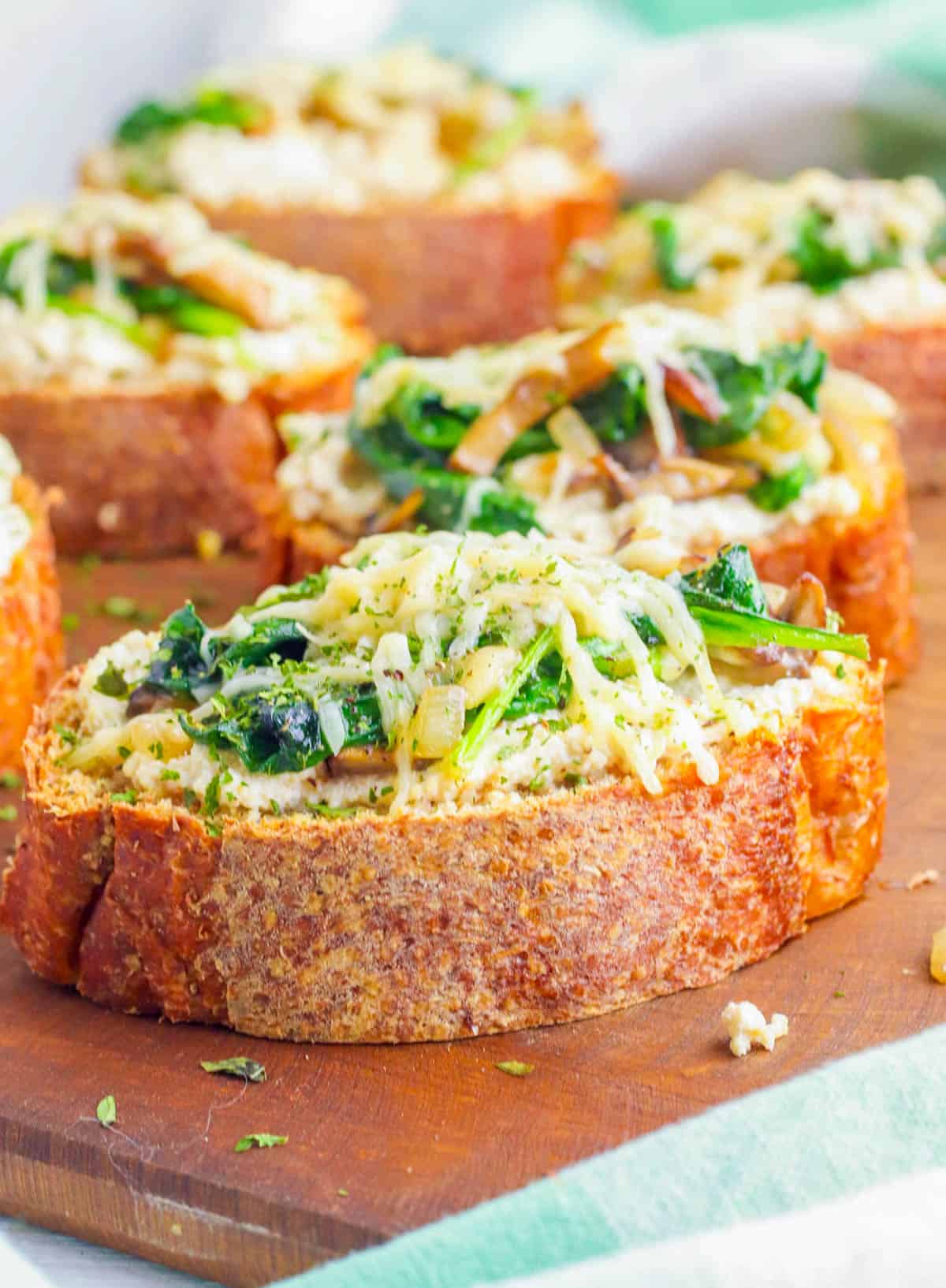 Mushroom toast with spinach and roasted garlic on a wooden cutting board.