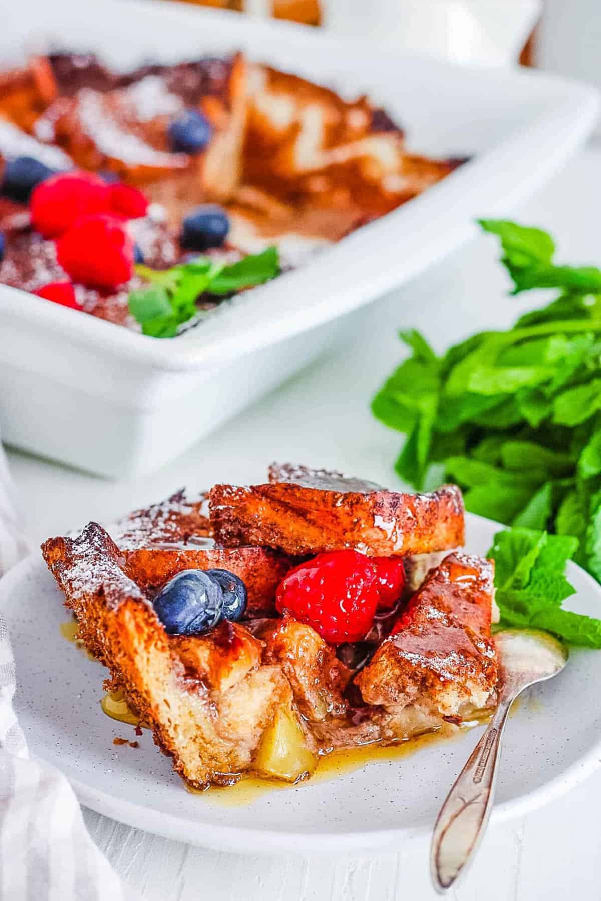 A closeup shot of a serving of vegan french toast casserole on a plate with berries and syrup. 