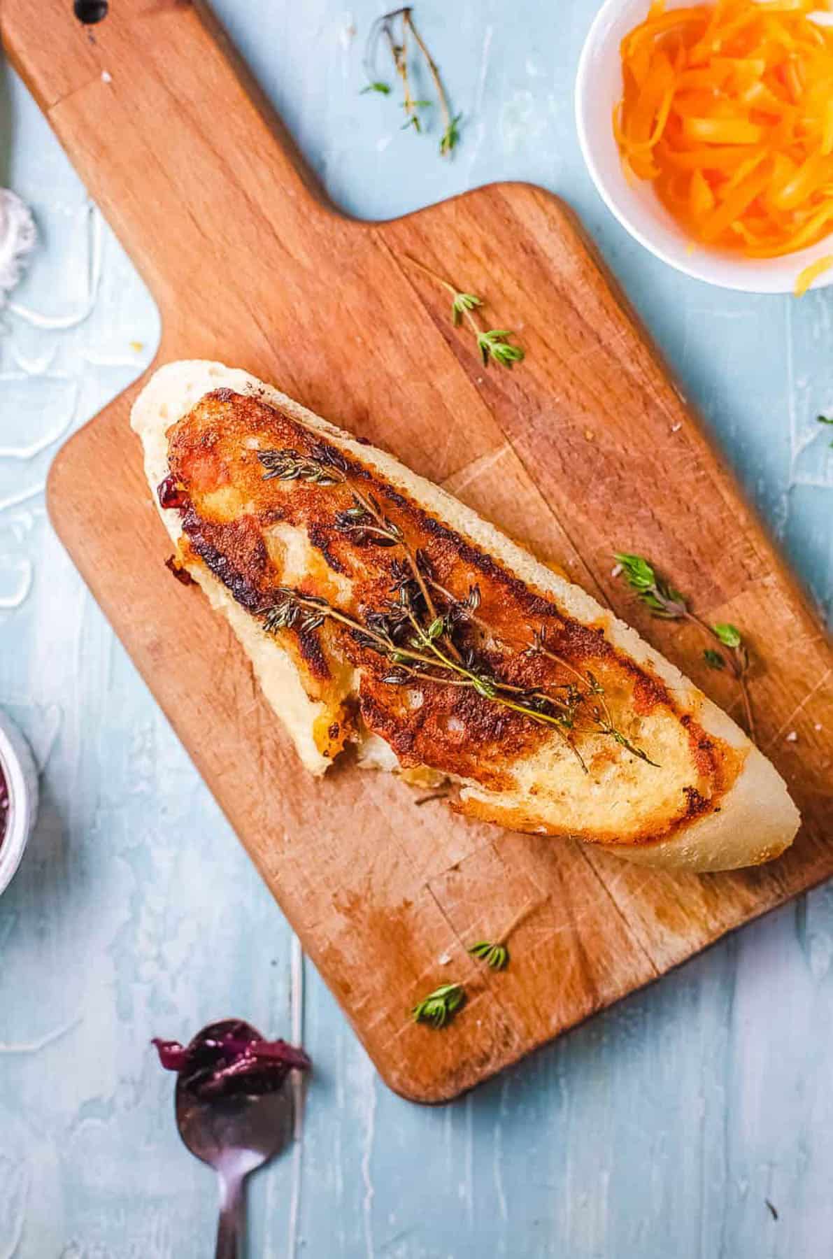 Overhead s،t of a wooden tray with a garlic bread grilled cheese sandwich on top.