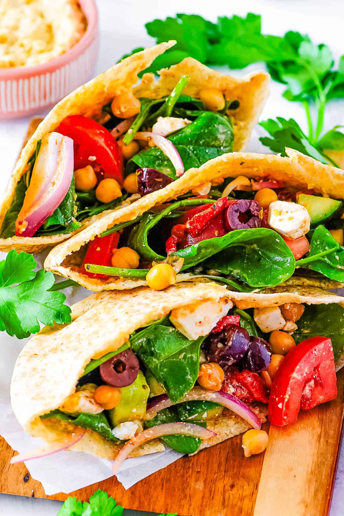 Greek pita sandwiches stuffed with veggies, feta, and chickpeas on a white cutting board.