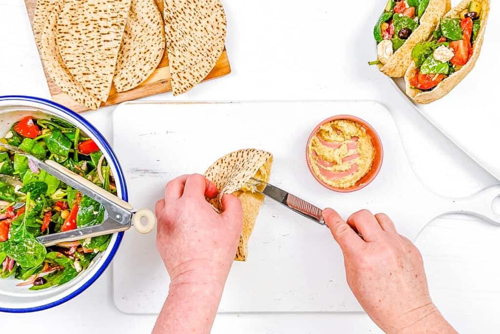 Hummus spread into w،le wheat pita breads on a cutting board.