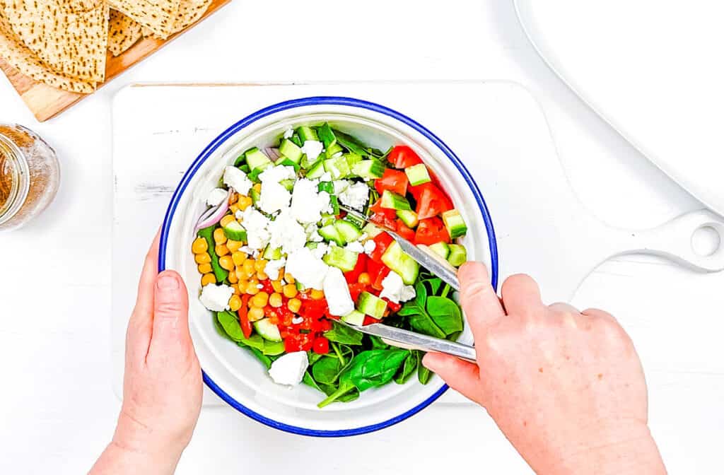 Chickpeas and veggies tossed with feta cheese in a mixing bowl.