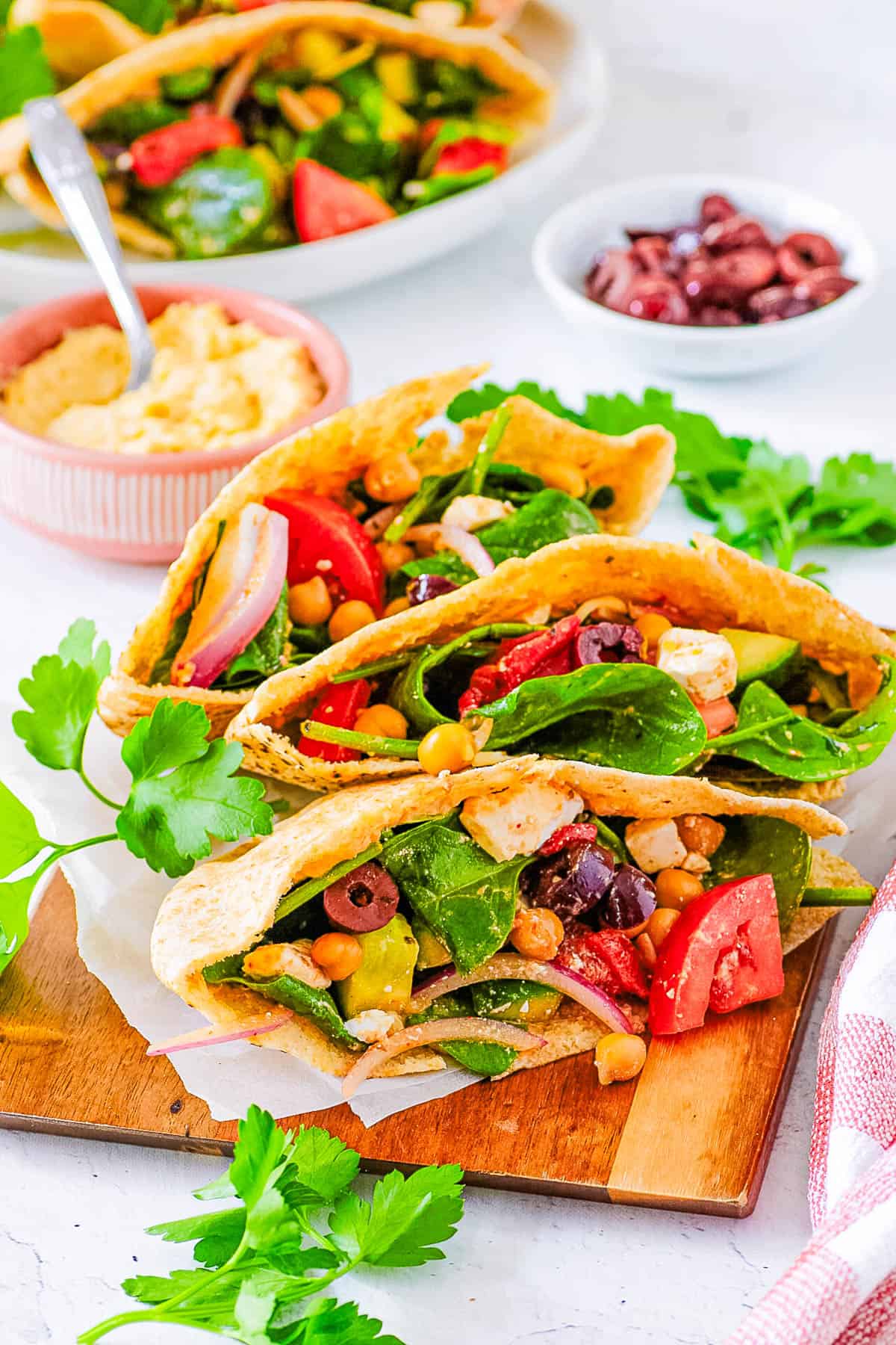 Vegetarian Greek pita sandwiches stacked on a wooden cutting board.