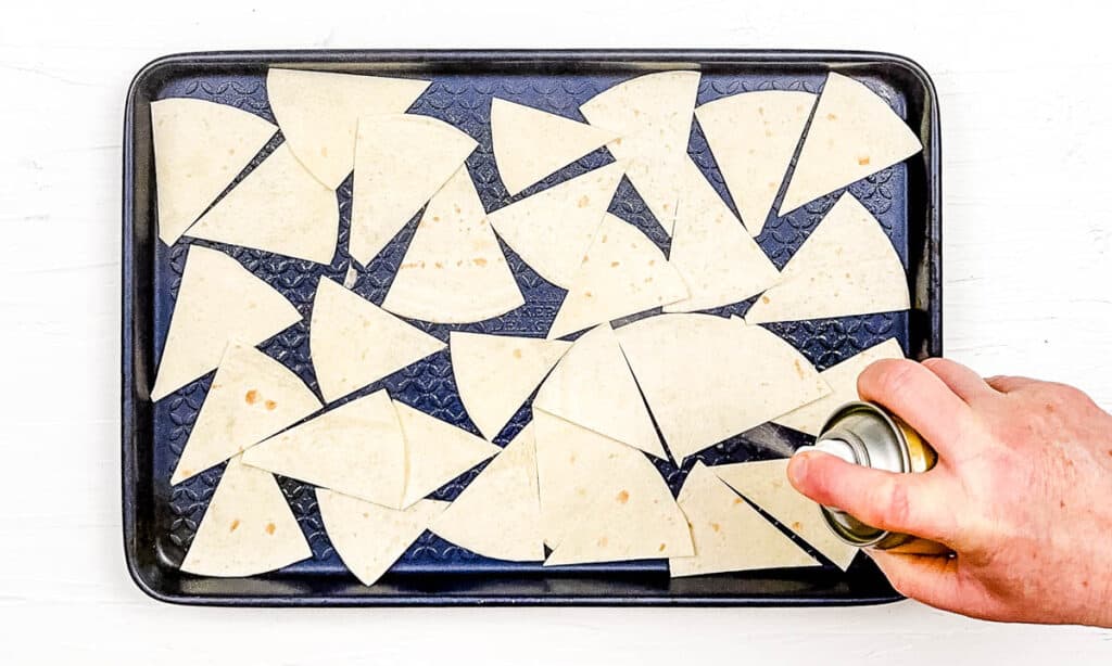 Tortilla wedges arranged on a baking sheet, sprayed with cooking spray.