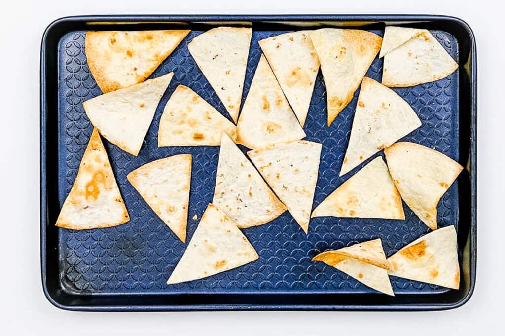 Baked tortilla chips on a baking sheet.