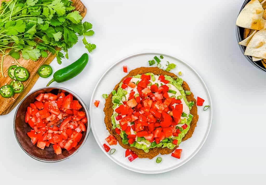 Tomatoes, Greek yogurt, mashed avocado, and refried beans layered on a white plate.