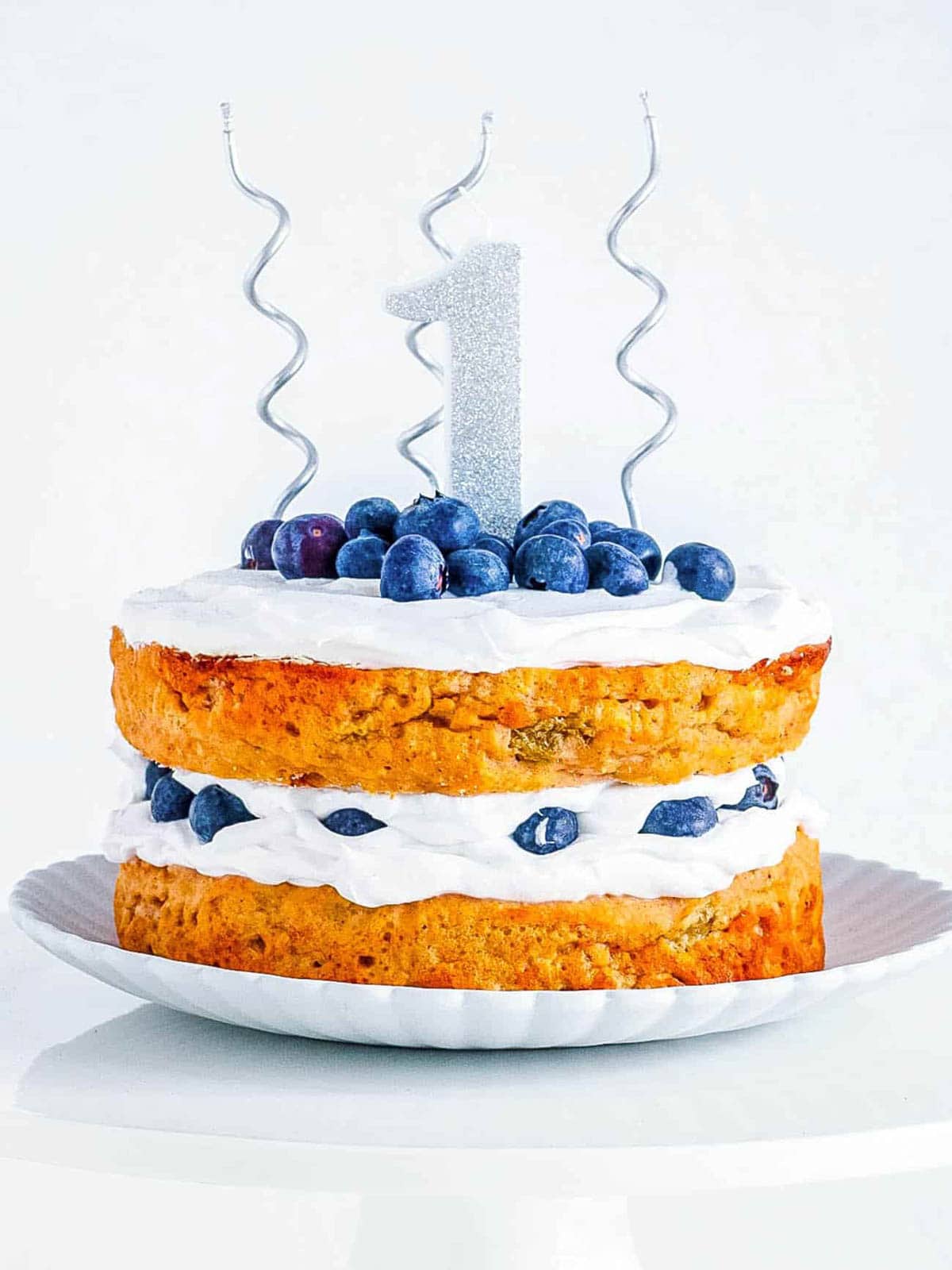 Healthy smash cake topped with blueberries and vegan frosting with 1st birthday decorations on top.