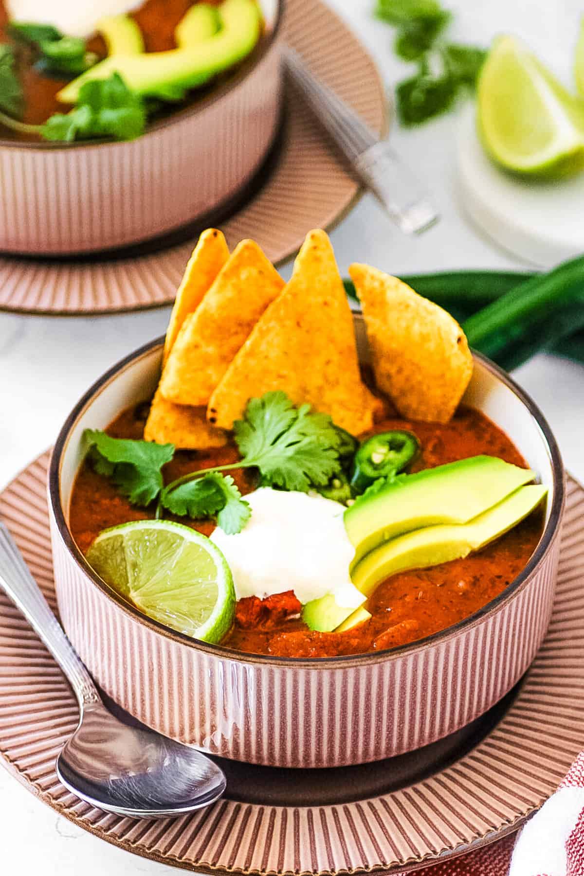 Easy vegan black bean soup, served in a grey bowl, garnished with cilantro, lime, avocado, crema, and corn chips.