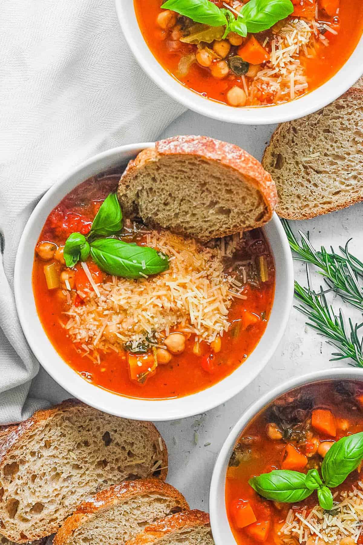 Italian chickpea soup served in a white bowl garnished with basil and with bread on the side.