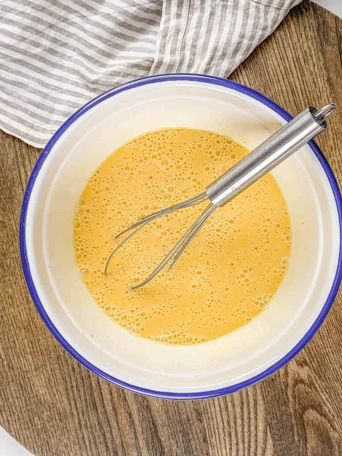 An overhead shot of a mixing bowl with a whisk and eggs.