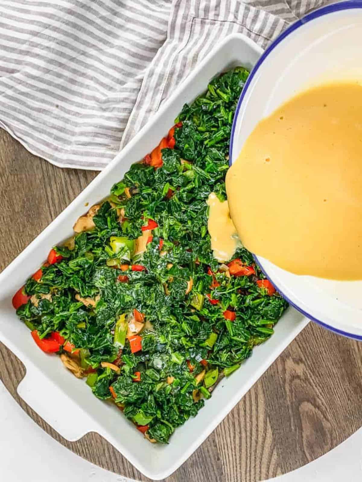Pouring beaten eggs over a white casserole dish of veggies.