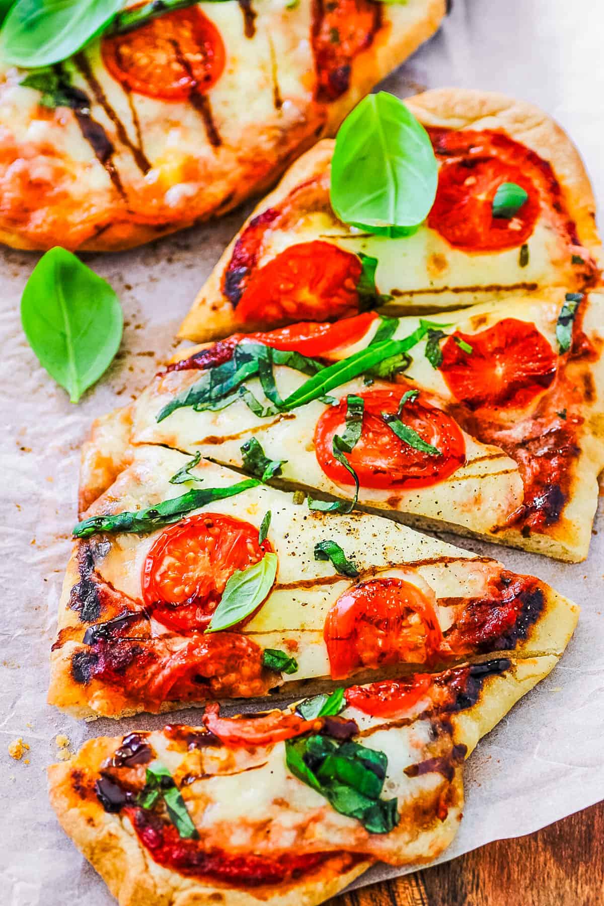 Margherita flatbread on a wooden cutting board, topped with basil, tomatoes and mozzarella.