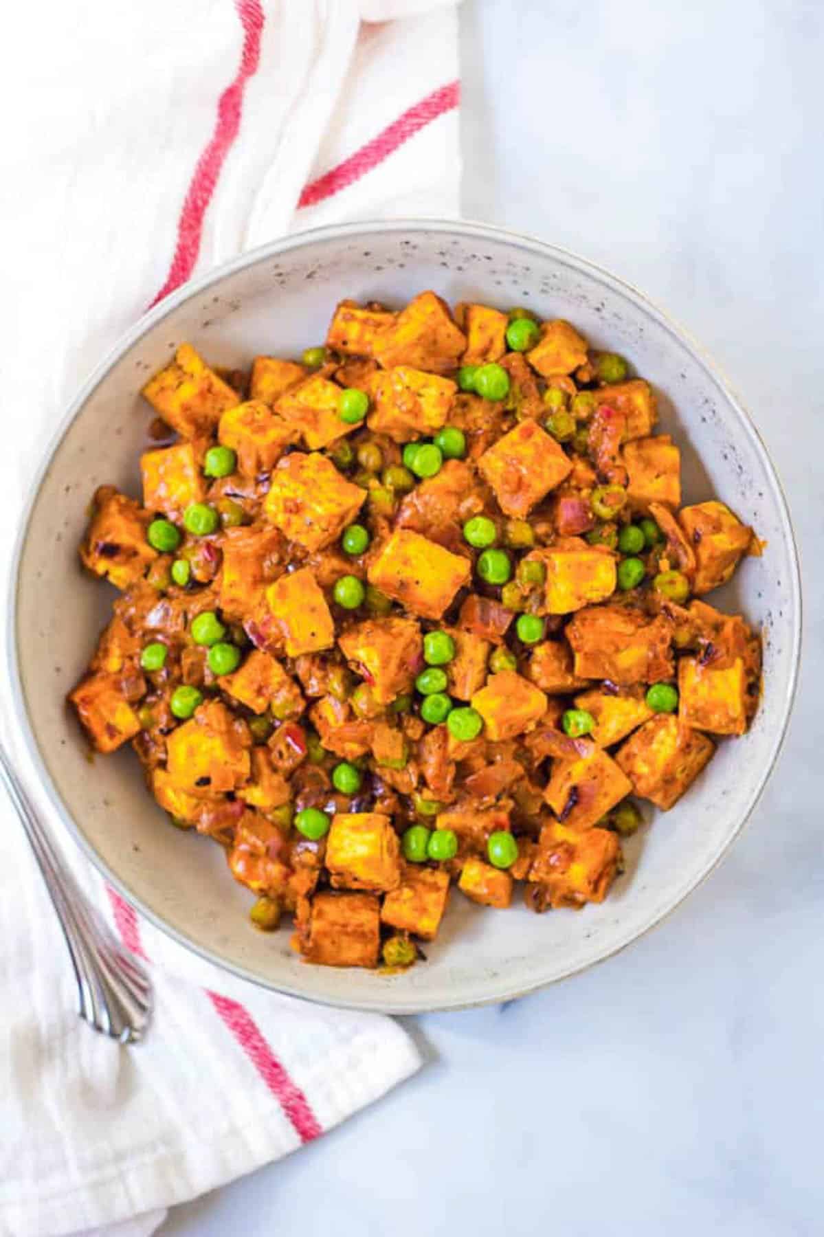 Overhead shot of a white bowl of mattar paneer with a napkin.