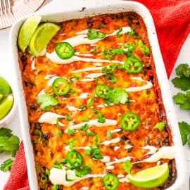 Mexican rice casserole, topped with cilantro, jalapeno slices and lime wedges, served in a white casserole dish.