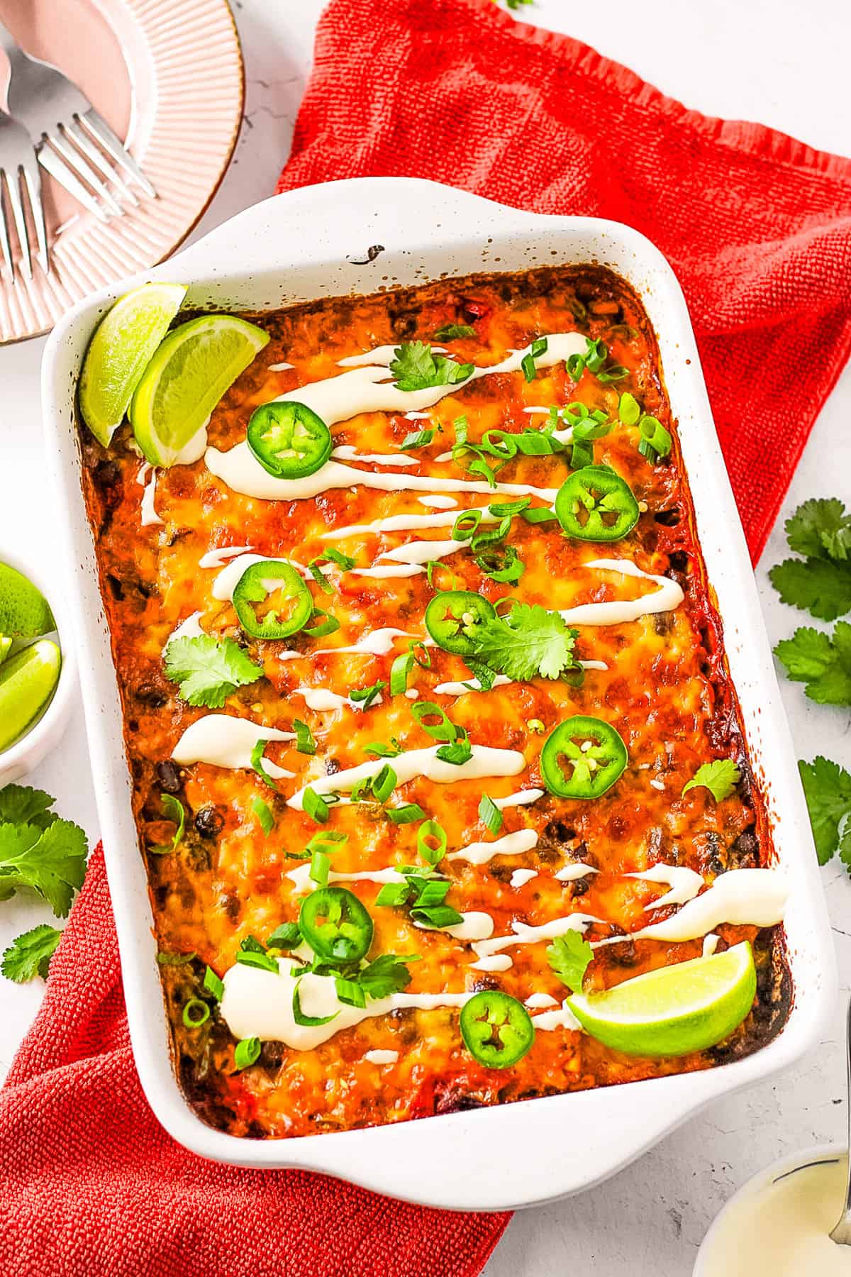 Mexican rice casserole, topped with cilantro, jalapeno slices and lime wedges, served in a white casserole dish.