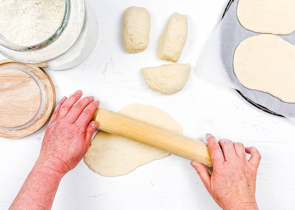 Dough for flatbread being rolled out on a white countertop.