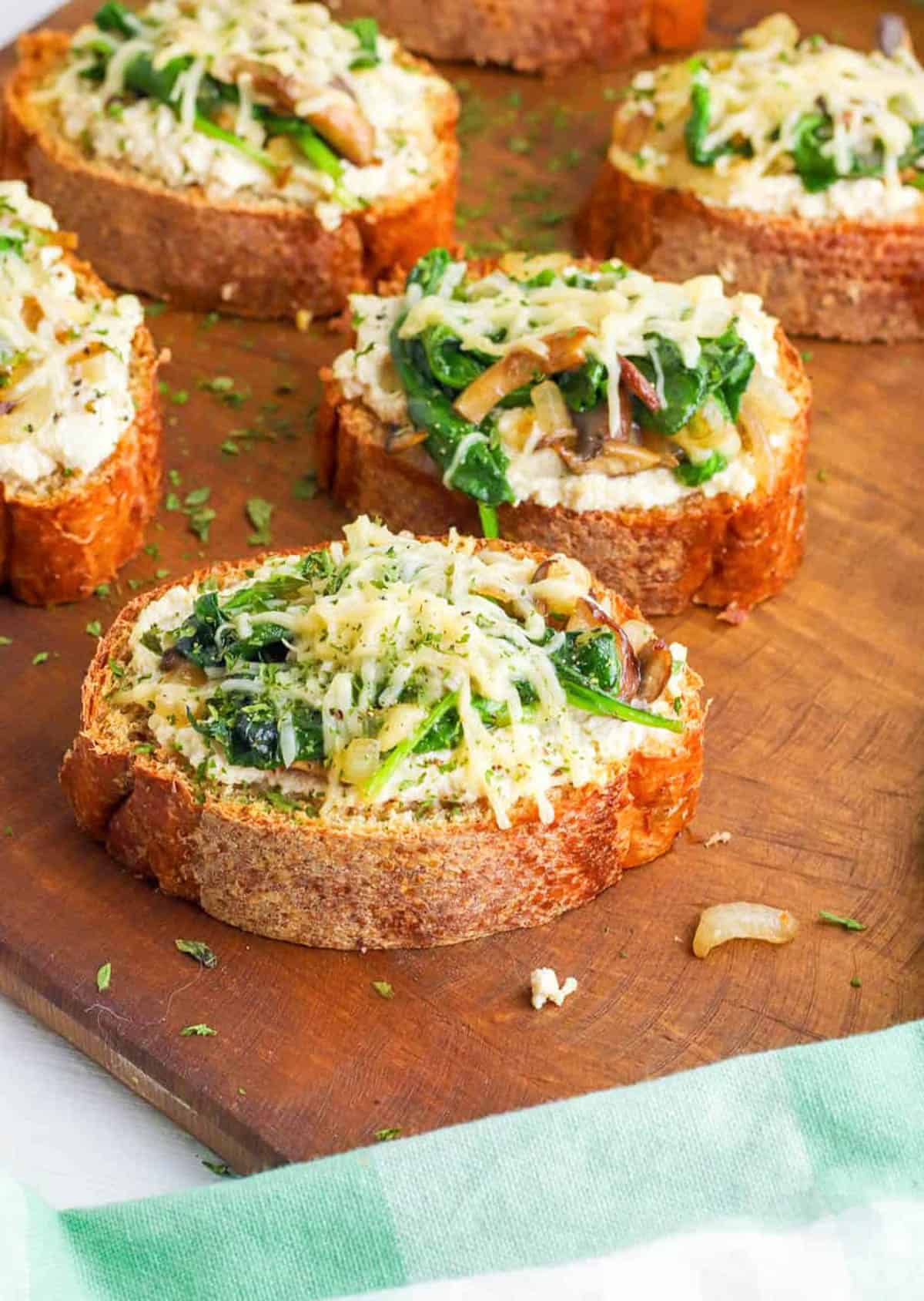 Mushroom toast with spinach and roasted garlic on a wooden cutting board.