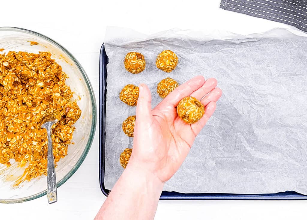 Pumpkin energy bites being rolled by hands and placed on a baking sheet.