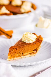 Slice of pumpkin apple pie on a white plate, topped with whipped cream.