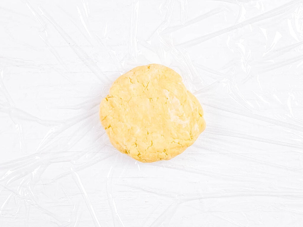 Pie dough being wrapped in plastic wrap to store in the fridge.