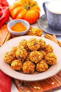 Pumpkin protein balls stacked on a white plate with fall decor in the background.