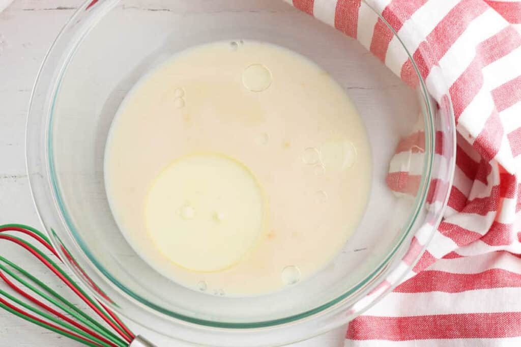 A mixing bowl of milk and oil with a whisk.