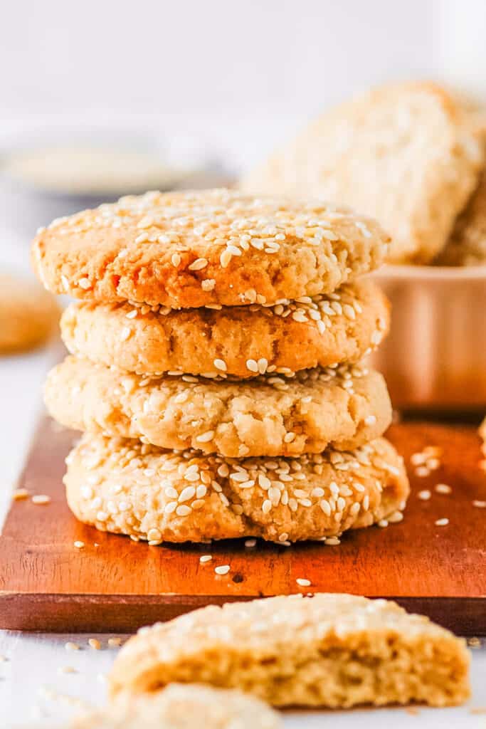 Sesame tahini cookies stacked on a wooden cutting board.