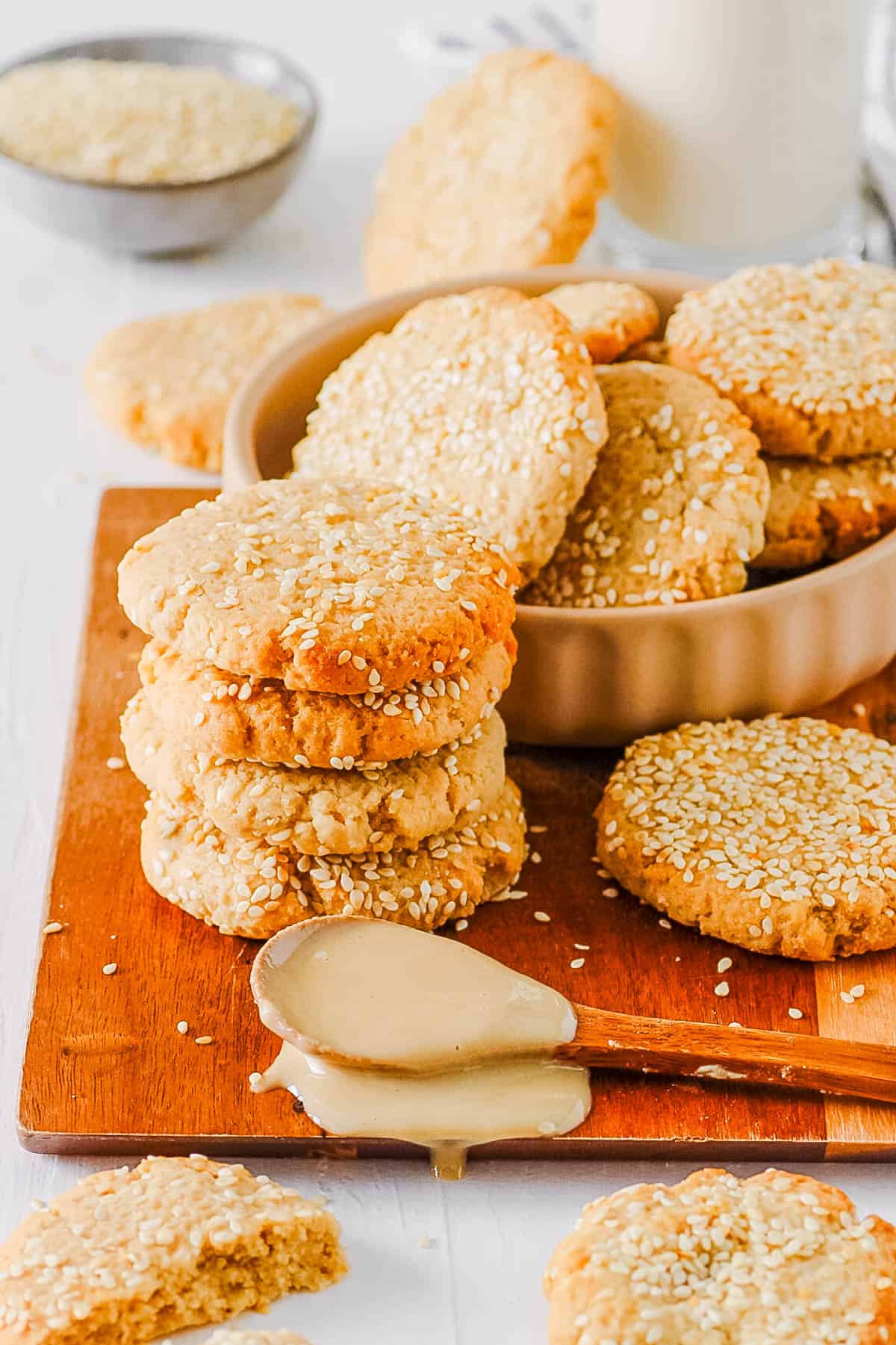 Sesame tahini cookies stacked on a wooden cutting board.