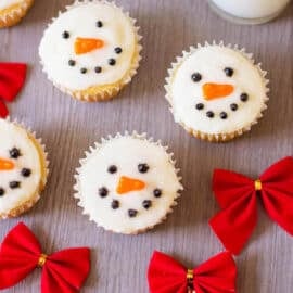 Decorated snowman cupcakes against a grey background with a glass of milk on the side.