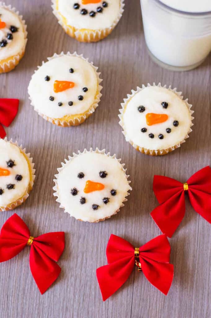 Decorated snowman cupcakes against a grey background with a glass of milk on the side.