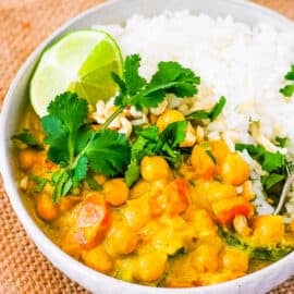 Thai peanut curry, served in a white bowl, with rice on the side, garnished with cilantro and lime.