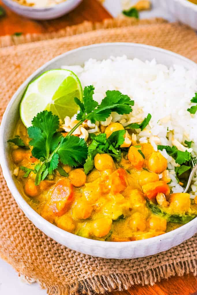 Thai peanut curry, served in a white bowl, with rice on the side, garnished with cilantro and lime.