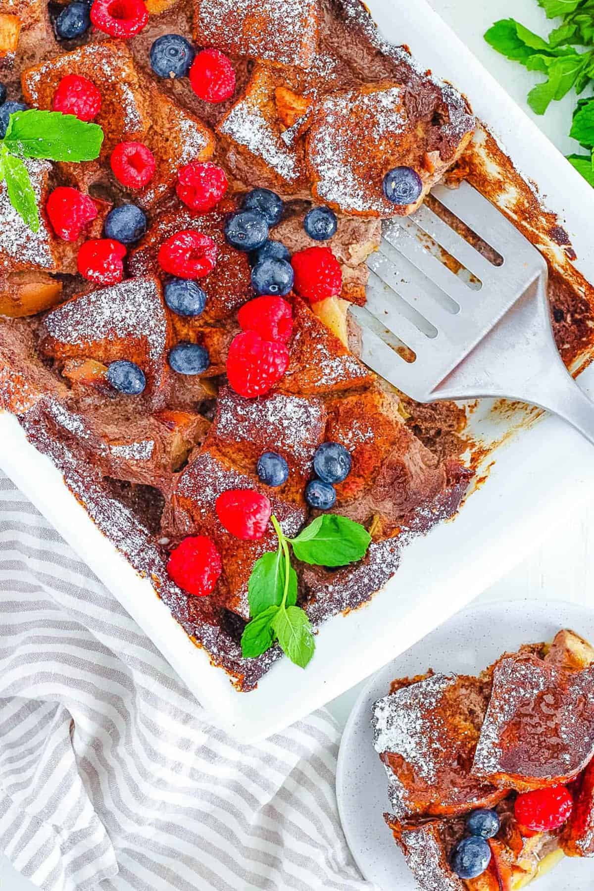 Overhead shot of a white pan of vegan french toast casserole with a serving spatula. 