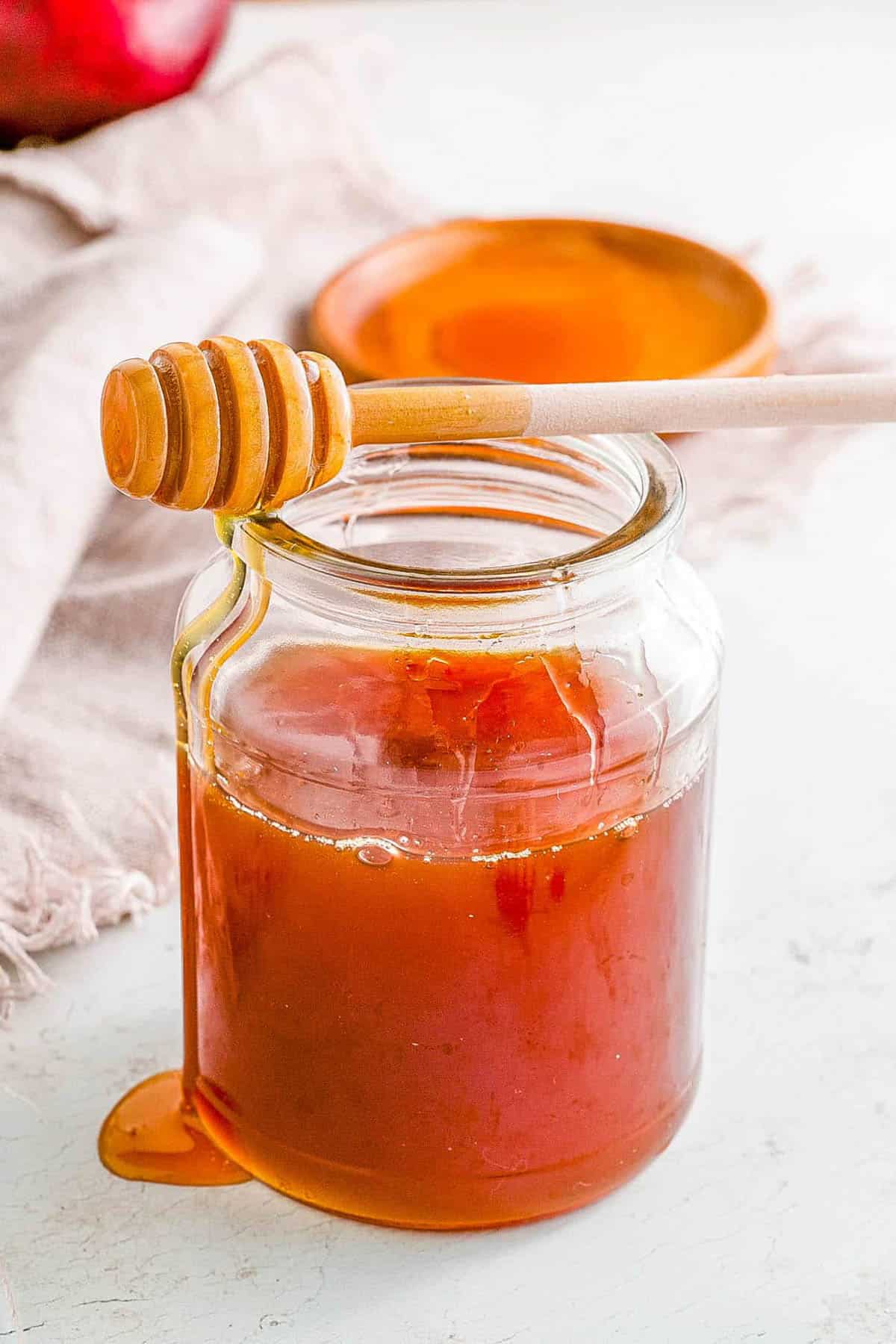 Jar of bee free honey with a honey dipper balanced on top.
