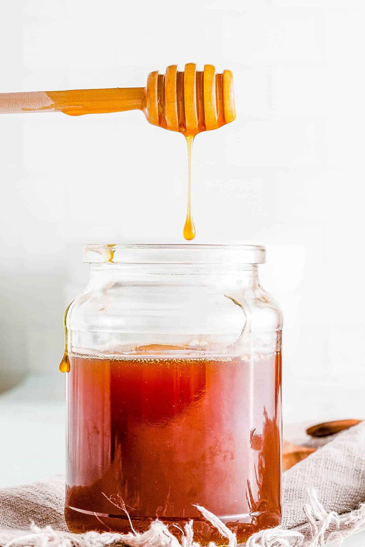 Jar of vegan honey with a honey dipper dipped inside, with honey dripping off of the dipper.