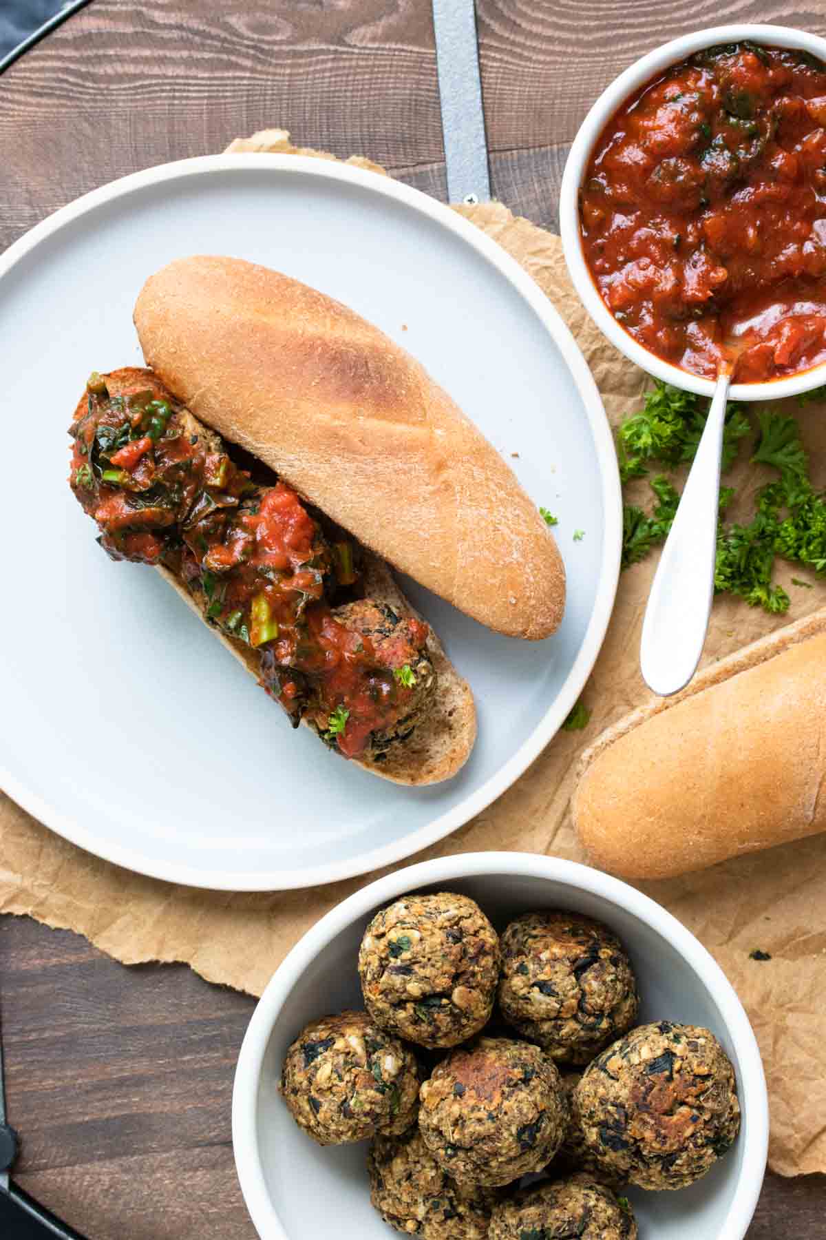 Open faced vegan meatball sub next to bowls of marinara and vegan meatballs.