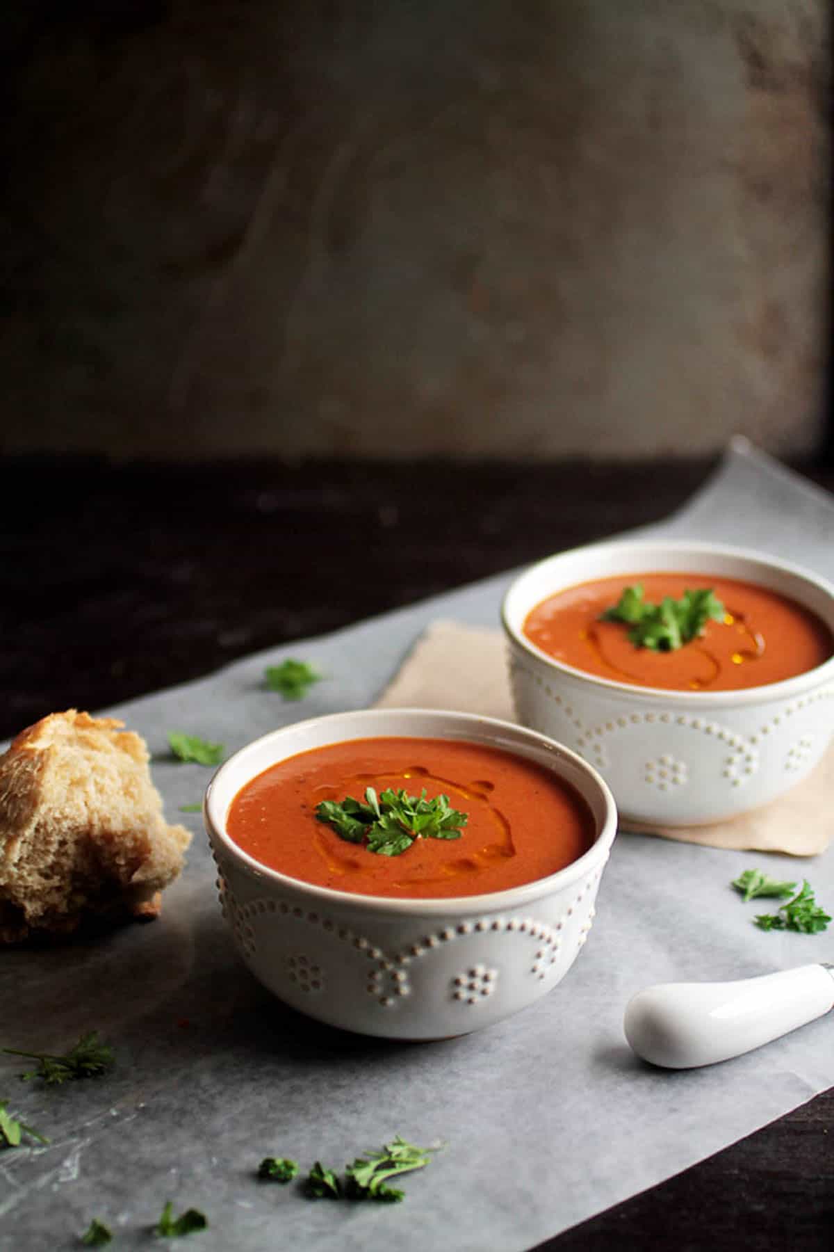 An angled shot of two white bowls of vegan red pepper soup on the counter.