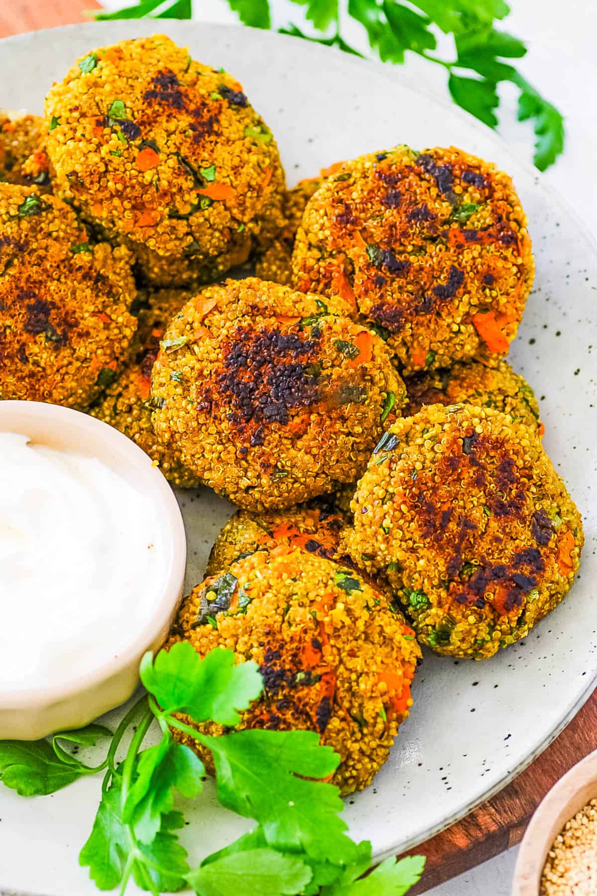 Vegan quinoa patties, stacked on a white plate, served with dipping sauce.