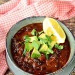 Vegan soup recipes - bowl of vegan black bean soup with avocado and lime as a garnish.