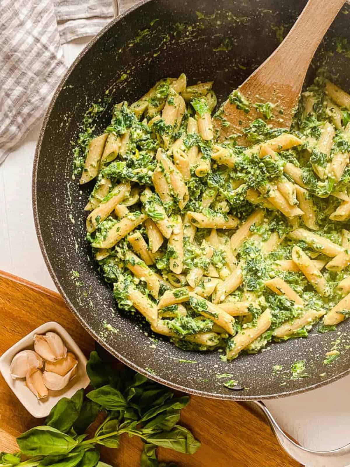 Overhead shot of a pan of vegetarian pesto pasta with a wooden spoon.