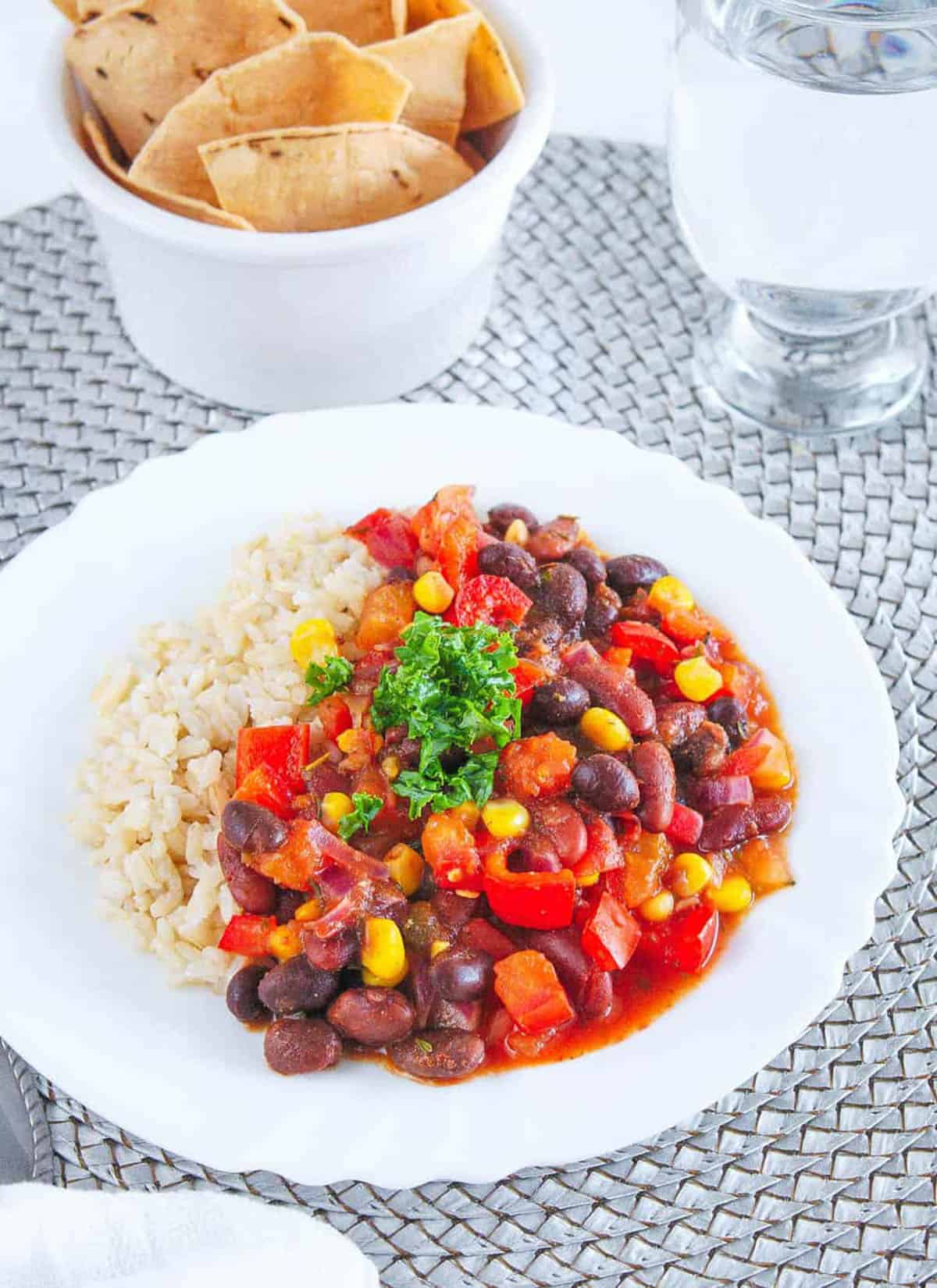 Beans and brown rice served on a white plate with corn and salsa.